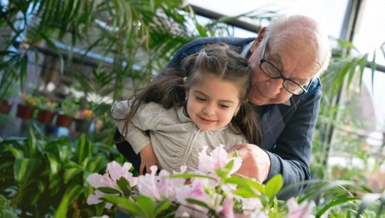 Grandparent teaching his granddaughter about plants and flowers at a greenhouse