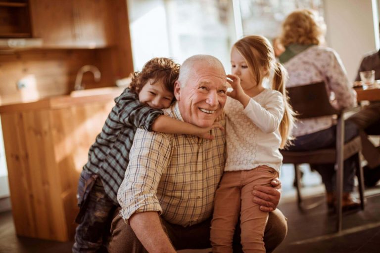 A man is wrestling and playing with two young children in the kitchen