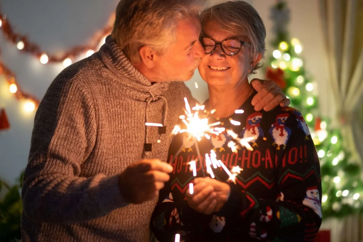 A couple lighting sparklers and wearing holiday sweaters