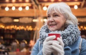 A woman holding a cup of warm drink and watching the holiday lights glisten