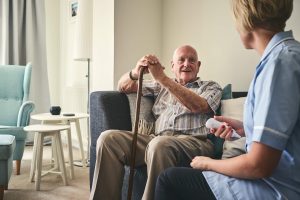 A man with a walking cane sits on acouch and talks witha nurse