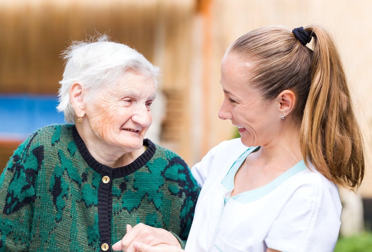 Caregiver smiling and aiding an older woman with dementia